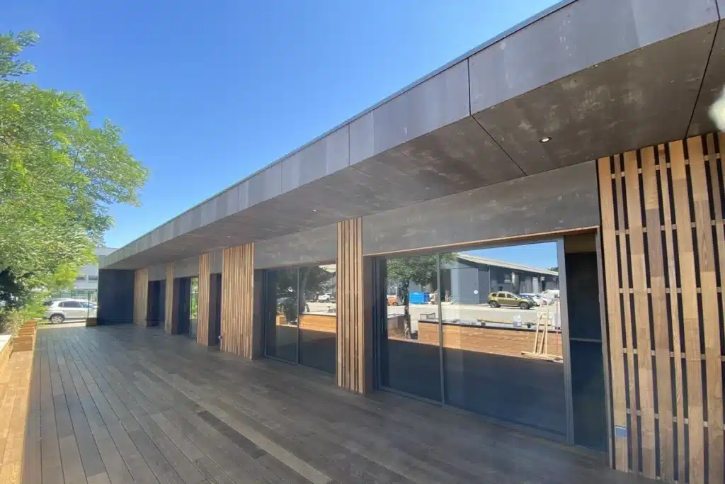 Façade d'un bâtiment avec des murs en verre et un sol en bois, mettant en valeur un bardage composite moderne.