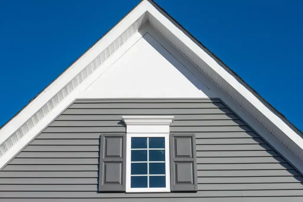 Façade d’une maison équipée d’un bardage PVC gris et de volets assortis, offrant un rendu moderne et durable.
